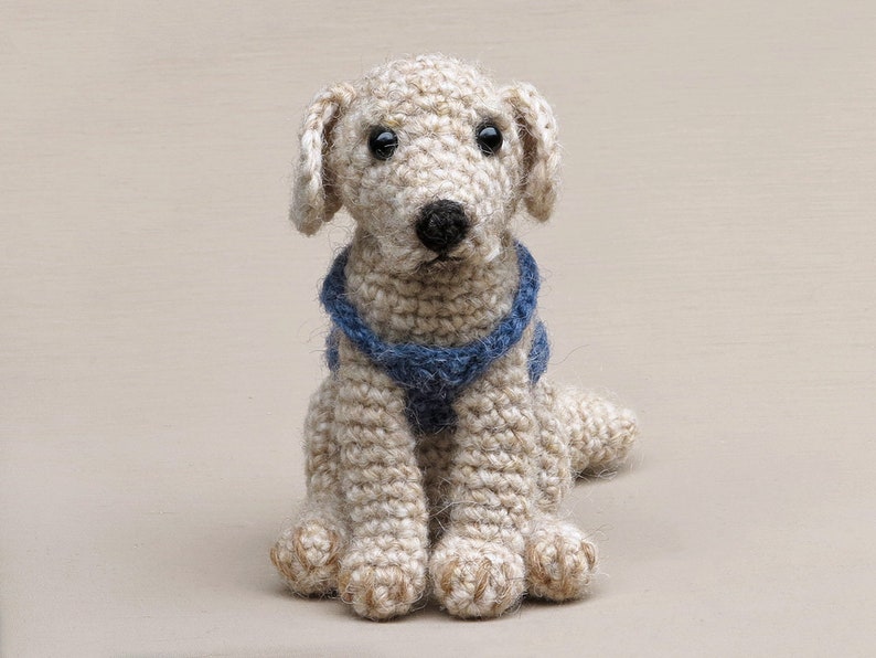 May include: A crocheted dog toy with a blue and white striped collar. The dog is sitting with its front paws forward and its back legs tucked behind it.