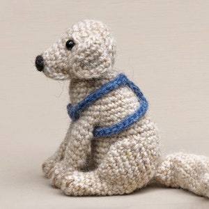 May include: A crocheted dog toy with a blue and white striped collar. The dog is sitting with its head turned to the side and its tail curled behind it.