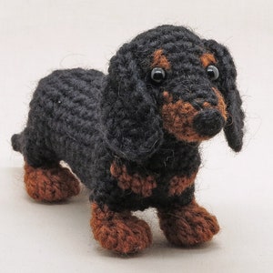 May include: A black and brown crocheted dachshund toy. The toy has black fur and brown legs and ears.