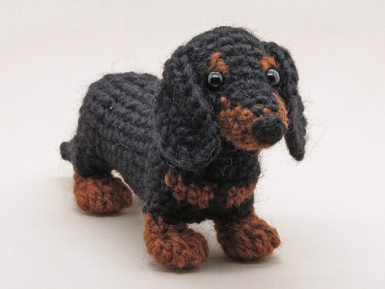 May include: A black and brown crocheted dachshund toy. The toy has black fur and brown legs and ears.