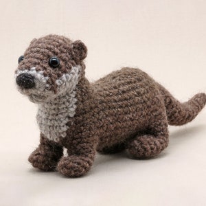 May include: A crocheted brown and white otter plush toy with black eyes. The otter is lying on its belly with its head turned to the side.