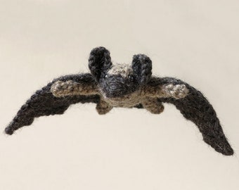 May include: A crocheted bat toy with brown and grey fur. The bat is in flight with its wings spread out.