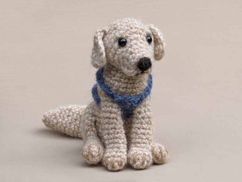May include: A crocheted cream-colored dog toy with a blue collar. The dog toy has a realistic face with black eyes and a black nose.