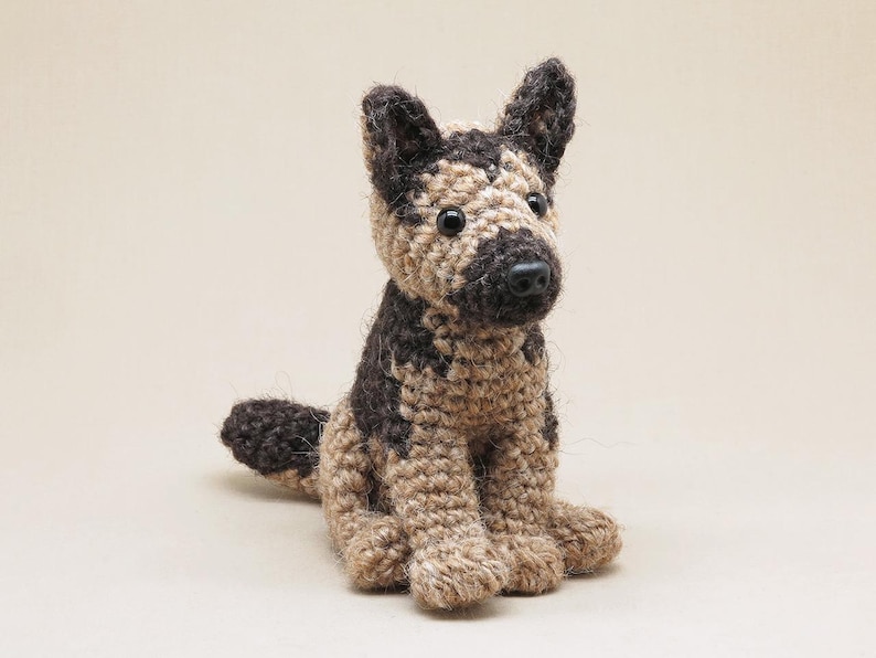 K&ouml;nnte beinhalten: Ein geh&auml;keltes Stofftier in Form eines Deutschen Sch&auml;ferhundes. Der Hund ist braun und schwarz mit einem braunen Gesicht und einer schwarzen Nase. Der Hund sitzt mit gekreuzten Beinen und seinem Schwanz hinter sich.