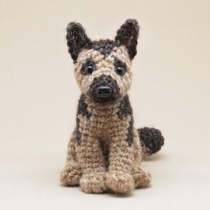 K&ouml;nnte beinhalten: Ein geh&auml;keltes Stofftier in Form eines Hundes mit braunem und braunem Fell. Der Hund sitzt mit den Pfoten unter dem K&ouml;rper und hat eine schwarze Nase und Augen.