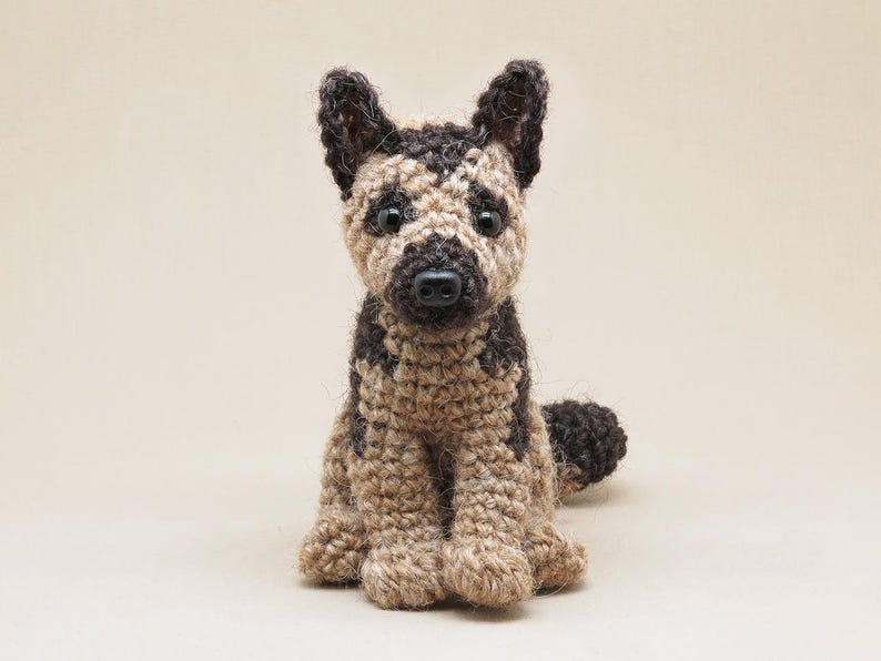 K&ouml;nnte beinhalten: Ein geh&auml;keltes Stofftier in Form eines Hundes mit braunem und braunem Fell. Der Hund sitzt mit den Pfoten unter dem K&ouml;rper und hat eine schwarze Nase und Augen.