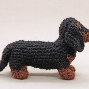 May include: A black and brown crocheted dachshund toy. The toy is made of yarn and has a long body and short legs.