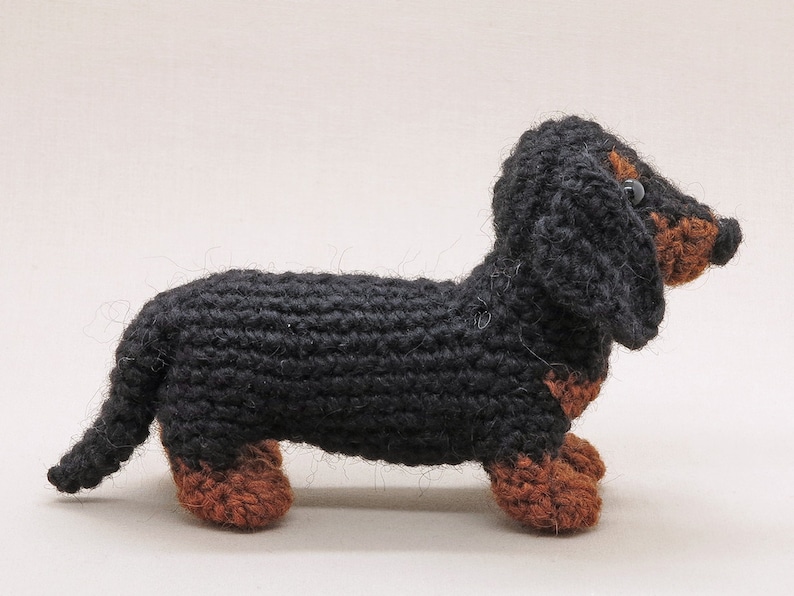 May include: A black and brown crocheted dachshund toy. The toy is made of yarn and has a long body and short legs.