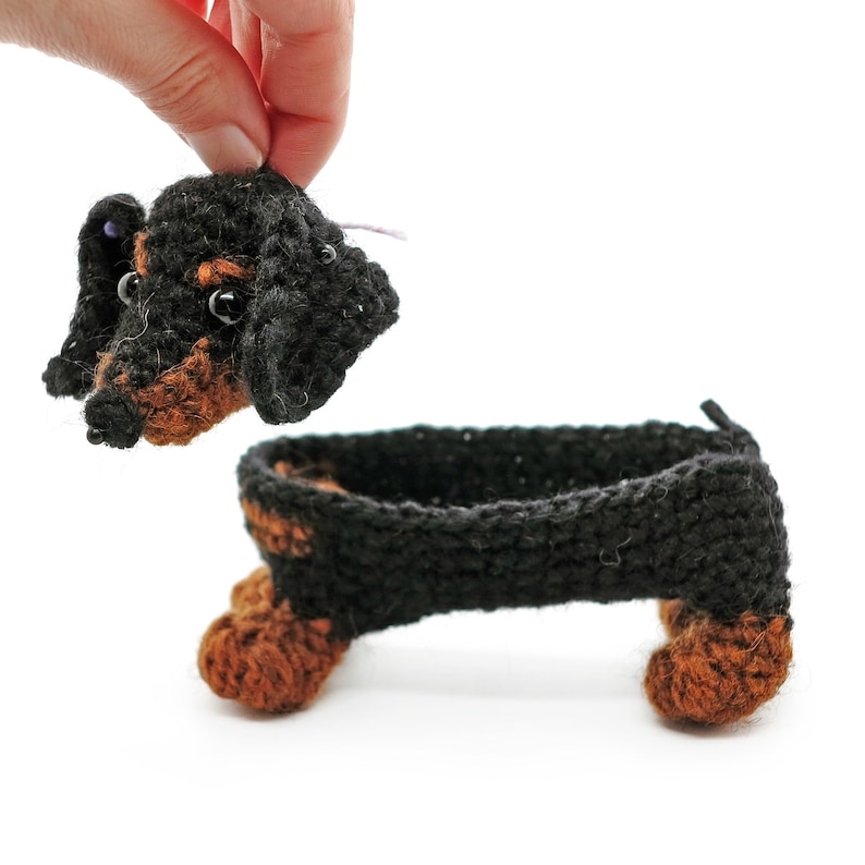 May include: A crocheted dachshund toy with black and brown fur. The toy is made of yarn and has a long body and short legs.
