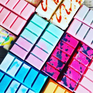 May include: Assortment of wax melts in various colors and patterns, including pink, blue, black, and white. The wax melts are arranged in a grid pattern.