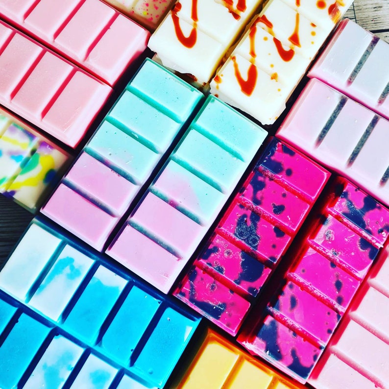 May include: Assortment of wax melts in various colors and patterns, including pink, blue, black, and white. The wax melts are arranged in a grid pattern.