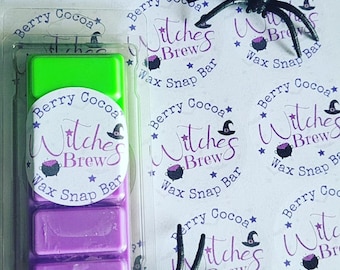 May include: A clear plastic package containing a wax snap bar with three rectangular sections, one green and two purple. The label reads "Berry Cocoa Witches Brew Wax Snap Bar." Several matching stickers and a black spider are also visible.