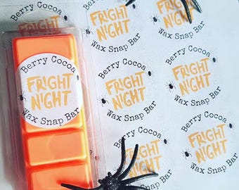 May include: An orange wax snap bar in a clear plastic package. The label reads "Berry Cocoa Fright Night Wax Snap Bar." Black plastic spiders are scattered around the wax melt. The theme is Halloween.