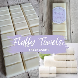 May include: A set of white wax melt snap bars with the text "Berry Cocoa Fluffy Towels Wax Snap Bar" on one bar. The bars are arranged in a grid pattern on a wooden surface. The text "Fluffy Towels Fresh Scent" is superimposed on the image. A stack of white towels is shown in the background.