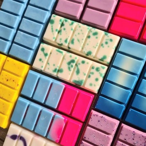May include: Assortment of colorful wax melts in various scents. The wax melts are arranged in a grid pattern and feature different colors, including blue, pink, yellow, and purple.