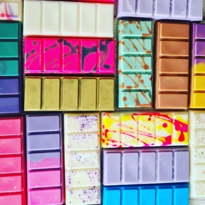 May include: Assortment of colorful wax melts in various patterns and colors, including purple, pink, green, yellow, and white. The wax melts are arranged in a grid pattern.
