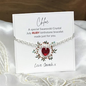 May include: A silver chain bracelet featuring a red heart-shaped Swarovski crystal charm. The bracelet is displayed on a white card with the text: Chloe, A special Swarovski Crystal July RUBY birthstone bracelet made just for you. Love Sarah x.