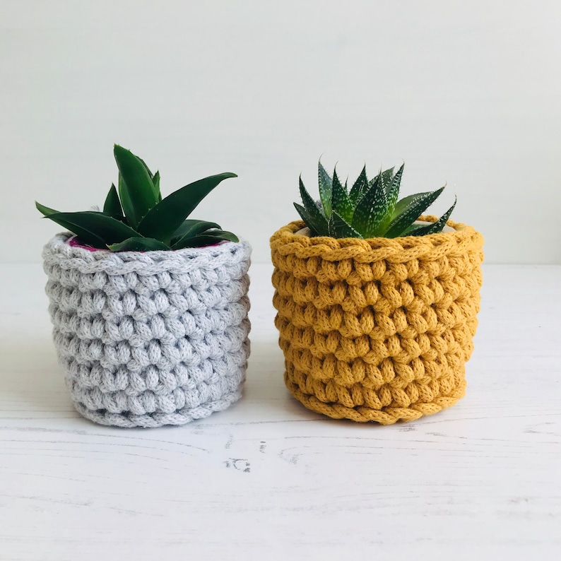 May include: Two crocheted plant pots, one gray and one yellow, with small green plants inside.