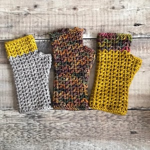 May include: Three pairs of crocheted fingerless gloves in different colors and patterns. The gloves are made with a variety of yarns, including a gray yarn, a multi-colored yarn, and a yellow yarn.