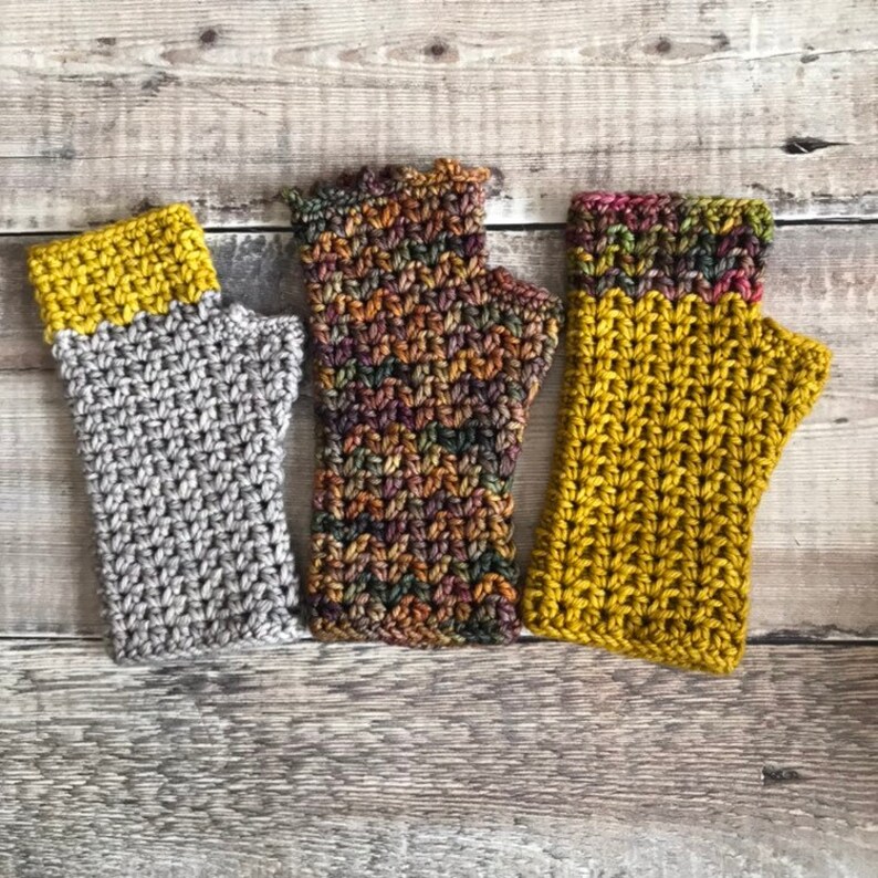May include: Three pairs of crocheted fingerless gloves in different colors and patterns. The gloves are made with a variety of yarns, including a gray yarn, a multi-colored yarn, and a yellow yarn.