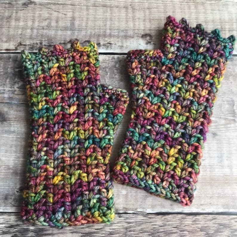 May include: A pair of colorful crocheted fingerless gloves with a textured pattern. The gloves are made with a multi-colored yarn that includes shades of green, purple, brown, and yellow.