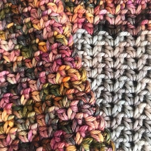 May include: Close-up of a crocheted fabric with two different patterns. One side is a multi-colored pattern with shades of pink, orange, brown, and green. The other side is a simple gray pattern.