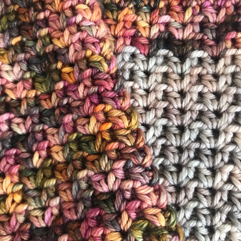 May include: Close-up of a crocheted fabric with two different patterns. One side is a multi-colored pattern with shades of pink, orange, brown, and green. The other side is a simple gray pattern.