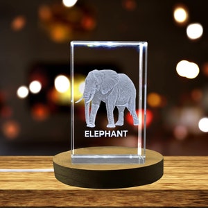 May include: A clear glass cube with an etched image of an elephant and the word "ELEPHANT" below it. The cube is lit from within and sits on a wooden base.