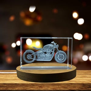 May include: A clear glass cube with a 3D etched image of a motorcycle on a wooden base. The motorcycle is a classic style with a single seat and a chrome exhaust.