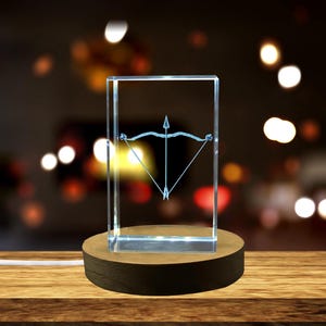 May include: A clear glass cube with a light inside, displaying a Sagittarius zodiac symbol. The cube is on a wooden base.