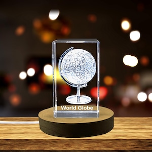 May include: A clear glass cube with a 3D etched image of a world globe on a stand. The cube is sitting on a wooden base and has the words "World Globe" printed on the bottom.