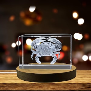 May include: A clear glass cube with a 3D etched image of a crab inside. The cube is sitting on a wooden base.