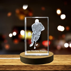 Op de afbeelding: Een kristallen kubus met een 3D-geëtst beeld van een ijshockeyer. De kubus staat op een houten voet en heeft een ingebouwde verlichting. De tekst "Ice Hockey Player" is op de voet gedrukt.