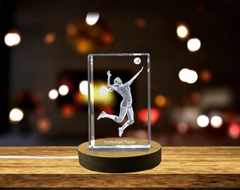 Può includere: Un cubo di cristallo trasparente con un'immagine incisa in 3D di un giocatore di pallavolo che schiaccia la palla. Il cubo è su una base di legno con una fonte di luce sottostante. Il testo "Volleyball Player" è inciso sulla base del cubo.