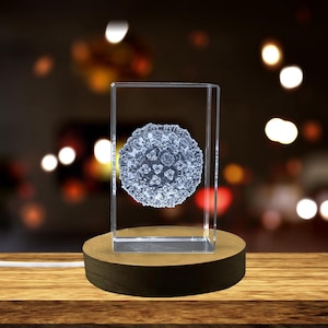 May include: A clear glass cube with a 3D etched image of a virus inside. The cube is on a wooden base with a light source underneath.