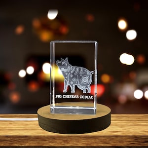 May include: A clear glass cube with a 3D etched image of a pig, the Chinese zodiac animal. The cube is on a wooden base and the text "PIG CHINESE ZODIAC" is engraved on the bottom of the cube.