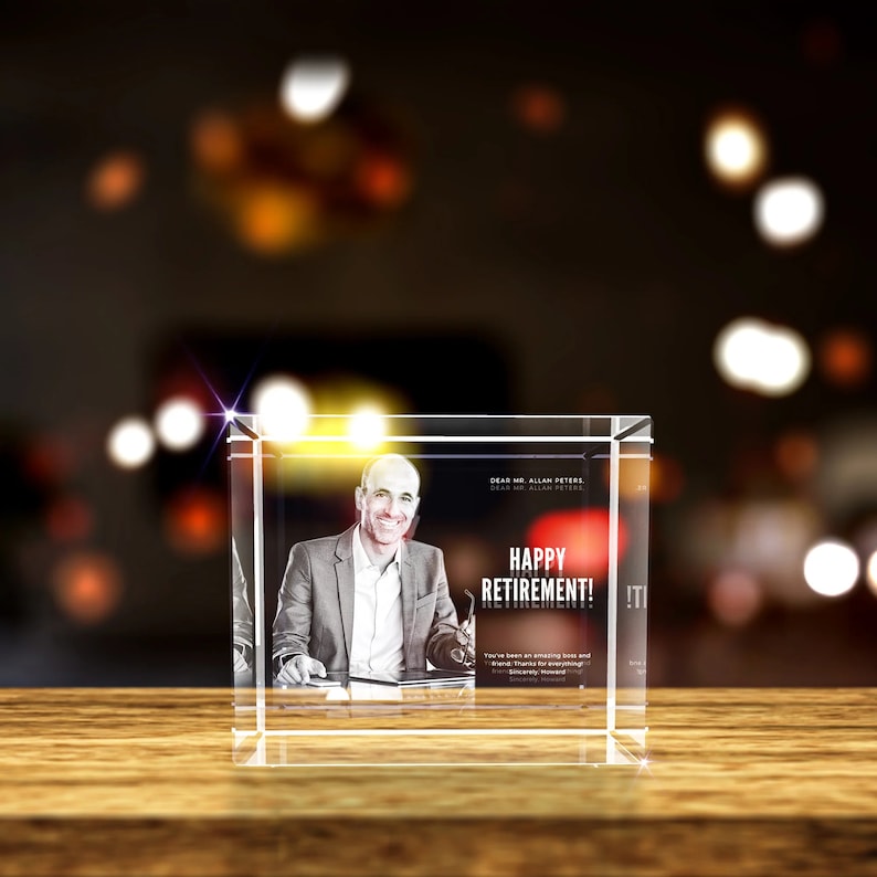 K&ouml;nnte beinhalten: Ein Kristallw&uuml;rfel mit einem 3D-gravierten Bild eines Mannes im Anzug und Krawatte. Der Text "Happy Retirement!" ist in Rot auf den W&uuml;rfel graviert. Der W&uuml;rfel steht auf einer Holzoberfl&auml;che.