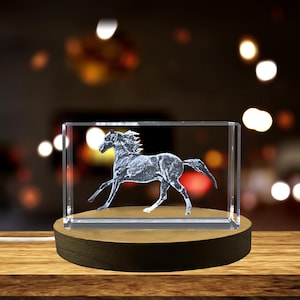 Pode incluir: Um peso de papel de cristal com uma imagem gravada em 3D de um cavalo correndo. O peso de papel está sobre uma base de madeira.