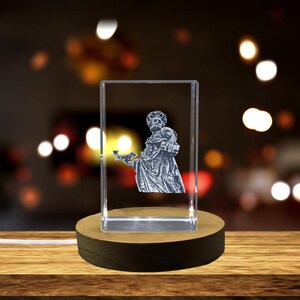 Peut inclure: Un cube de cristal avec une gravure laser 3D d'une personne tenant un oiseau. Le cube est sur une base en bois avec une source de lumière en dessous.