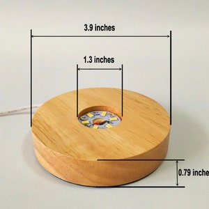 K&ouml;nnte beinhalten: Ein Holzdisplay mit einem runden Sockel und einem kleineren runden Ausschnitt in der Mitte. Der Sockel hat einen Durchmesser von 3,9 Zoll, ist 1,3 Zoll hoch und 0,79 Zoll dick. Er verf&uuml;gt &uuml;ber eine eingebaute LED-Leuchte im mittleren Ausschnitt.