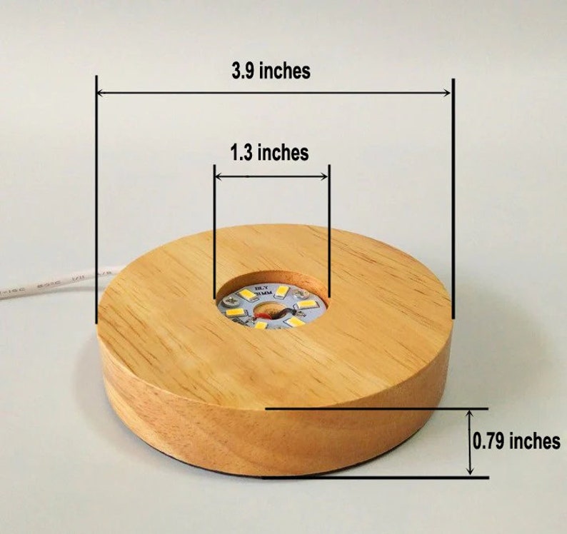 K&ouml;nnte beinhalten: Ein Holzdisplay mit einem runden Sockel und einem kleineren runden Ausschnitt in der Mitte. Der Sockel hat einen Durchmesser von 3,9 Zoll, ist 1,3 Zoll hoch und 0,79 Zoll dick. Er verf&uuml;gt &uuml;ber eine eingebaute LED-Leuchte im mittleren Ausschnitt.