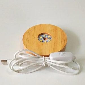 K&ouml;nnte beinhalten: Ein Holzsockel mit einer runden Aussparung f&uuml;r eine Kristallkugel. Der Sockel verf&uuml;gt &uuml;ber eine eingebaute LED-Leuchte mit einem USB-Kabel und einem Inline-Schalter. Das Licht ist wei&szlig;.