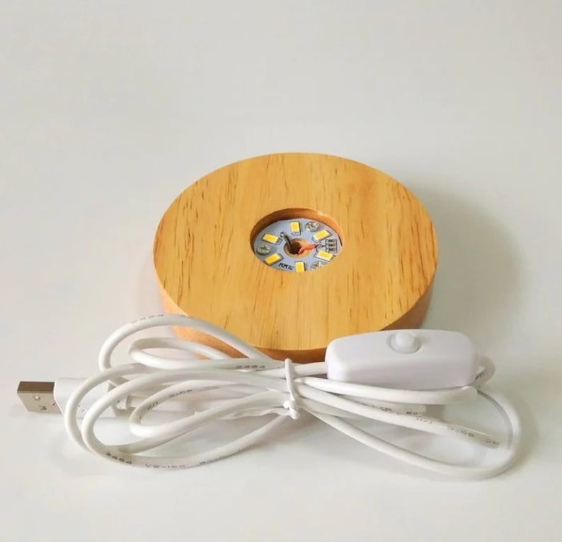 K&ouml;nnte beinhalten: Ein Holzsockel mit einer runden Aussparung f&uuml;r eine Kristallkugel. Der Sockel verf&uuml;gt &uuml;ber eine eingebaute LED-Leuchte mit einem USB-Kabel und einem Inline-Schalter. Das Licht ist wei&szlig;.