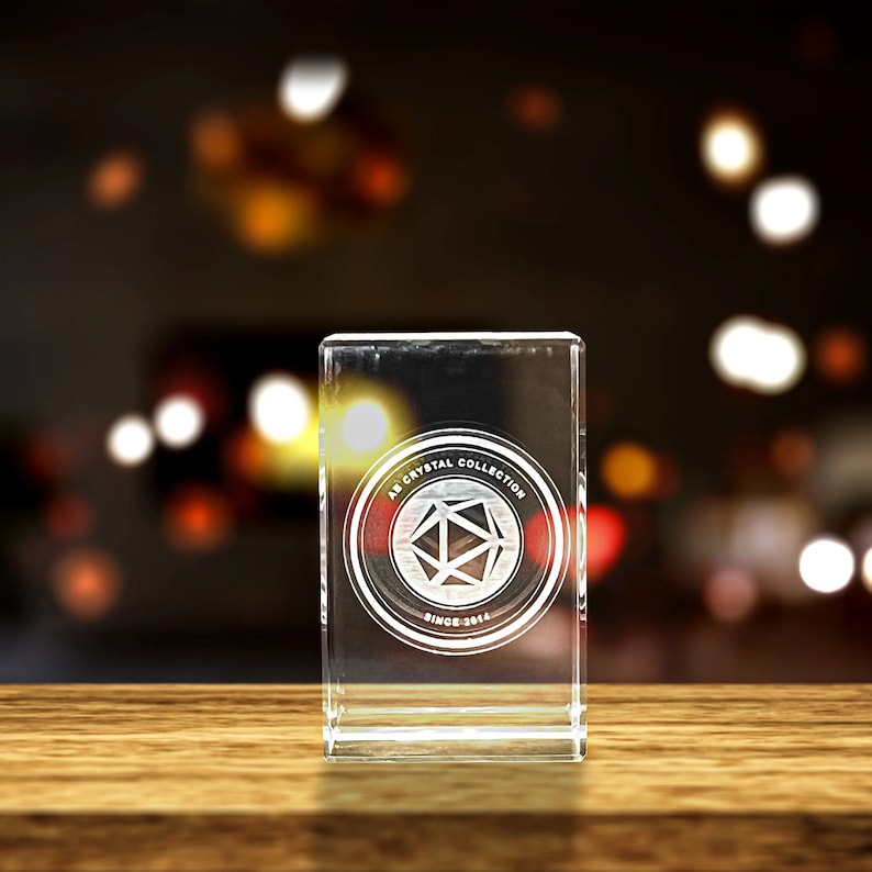 K&ouml;nnte beinhalten: Ein durchsichtiger Glas-Briefbeschwerer mit einem kreisf&ouml;rmigen Design, das den Text "AB Crystal Collection Since 2014" und eine geometrische Form im Kreis enth&auml;lt.
