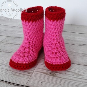 May include: A pair of pink and red crocheted slipper socks. The socks have a red trim around the top and bottom.