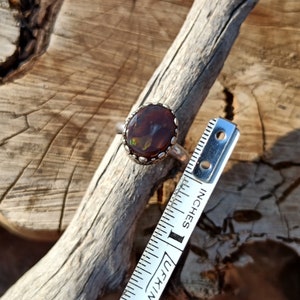 May include: A silver ring with a brown and green opal gemstone set in a silver bezel. The ring is shown next to a ruler measuring 1 inch.