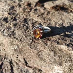 May include: A silver ring with a large, round, orange and brown gemstone set in a decorative silver bezel.