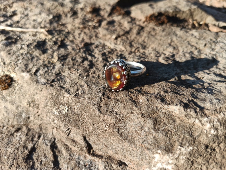 May include: A silver ring with a large, round, orange and brown gemstone set in a decorative silver bezel.