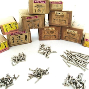 Op de afbeelding: Assortiment van kleine messing schroeven voor hout in verschillende maten, verpakt in kartonnen dozen met de labels "Nickel-Plated" en "Flat Head". De schroeven liggen verspreid op een wit oppervlak.
