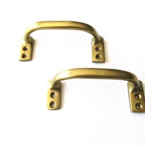 以下が含まれることがあります： シンプルな曲線デザインの真鍮製のドアハンドル2個。各ハンドルには、取り付け用のネジ穴が2つあります。